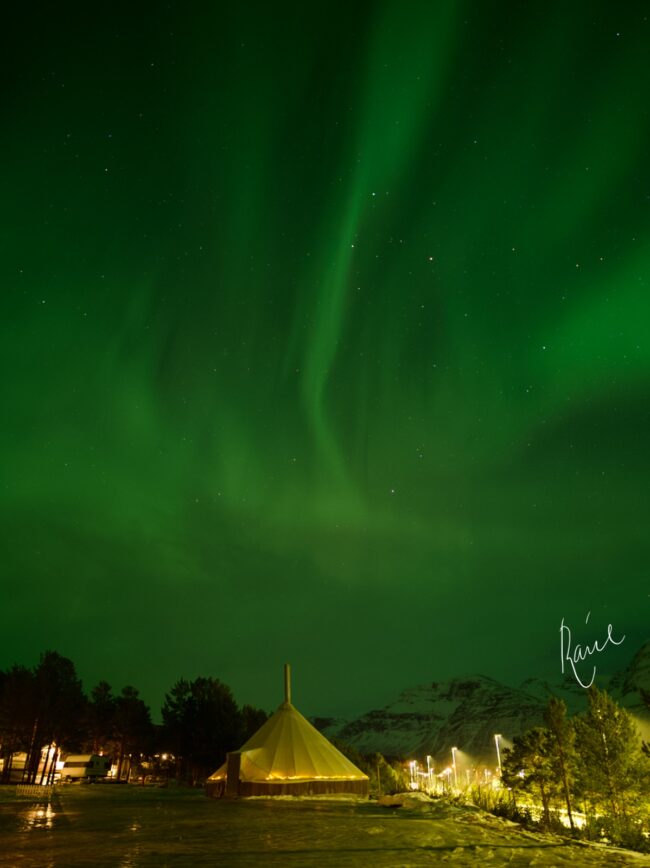 Green auroras above a triangular tent.