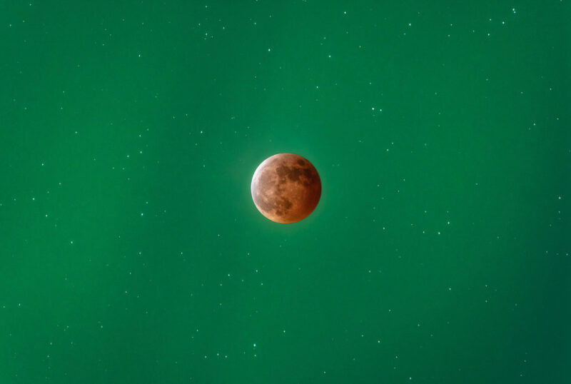 A reddish eclipsed moon on a green background.