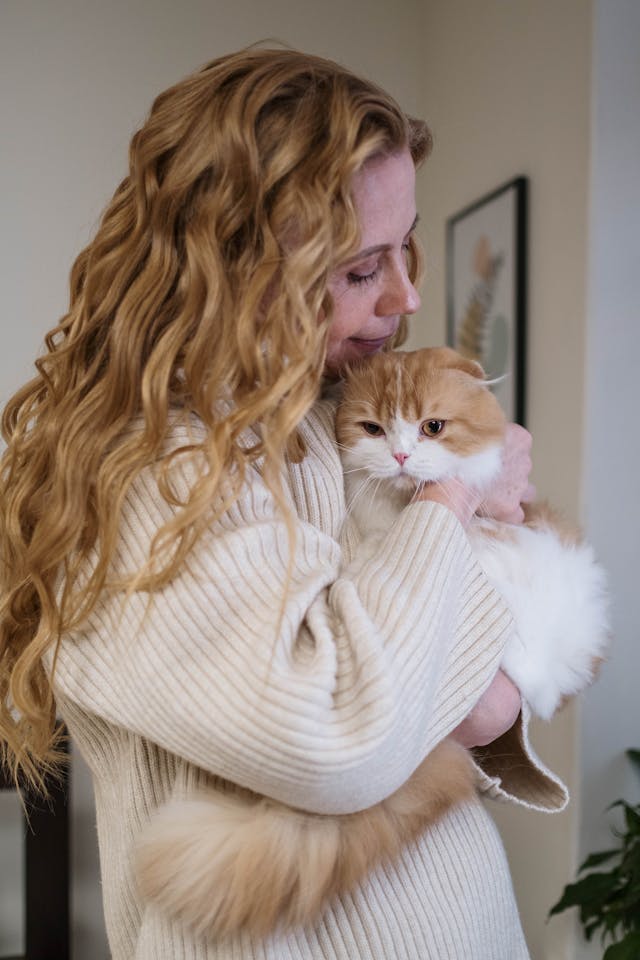 A woman with long curly hair snuggles an orange and white cat.