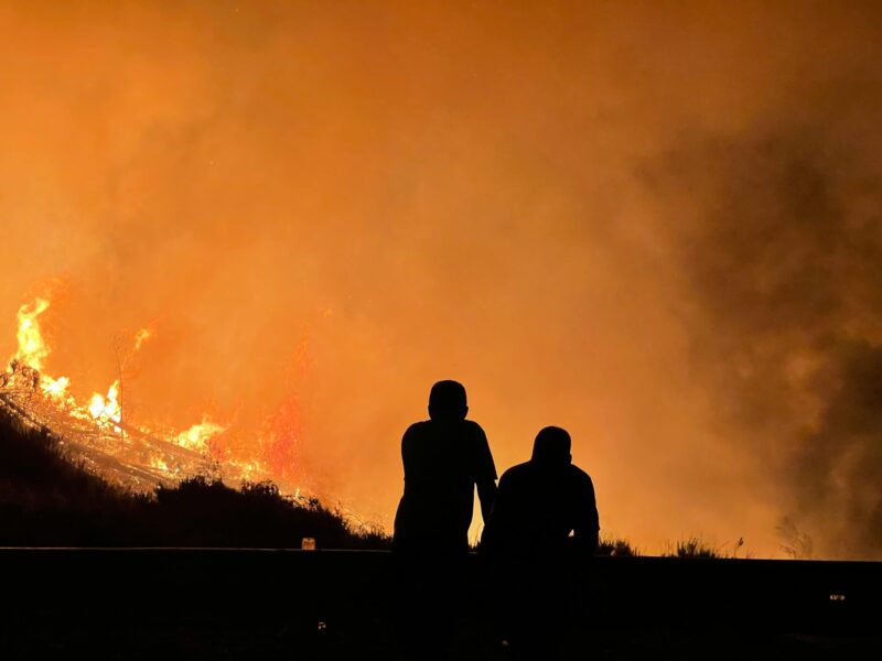 Two people in shadow looking at the orange glow of a wildfire.