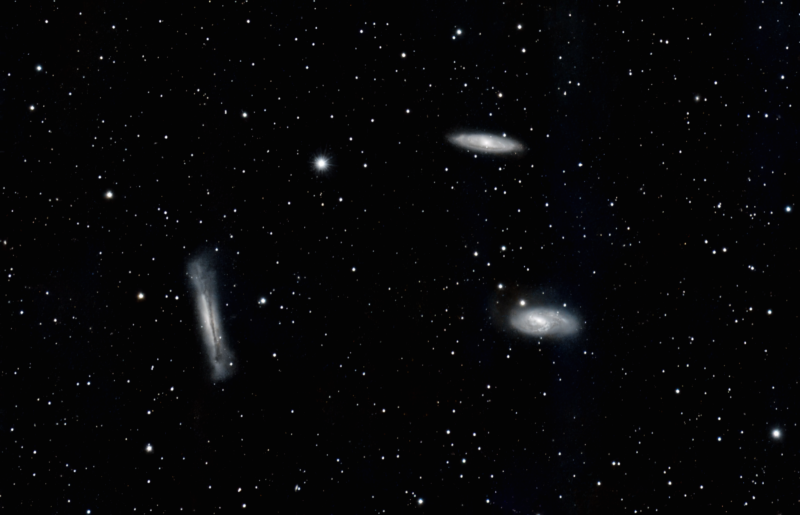Three mid-sized whitish clouds, one irregular and two spiral, over a rich foreground of stars.