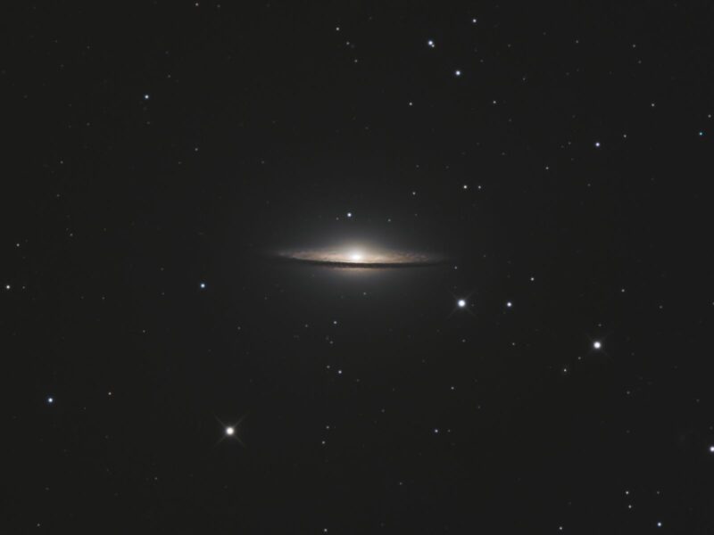 Yellowish hat-shaped galaxy seen edge-on, with a prominent dark lane and sparse foreground stars.
