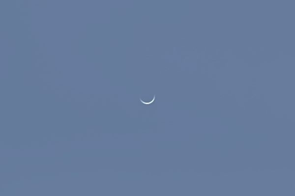A very thin crescent on a blue sky.