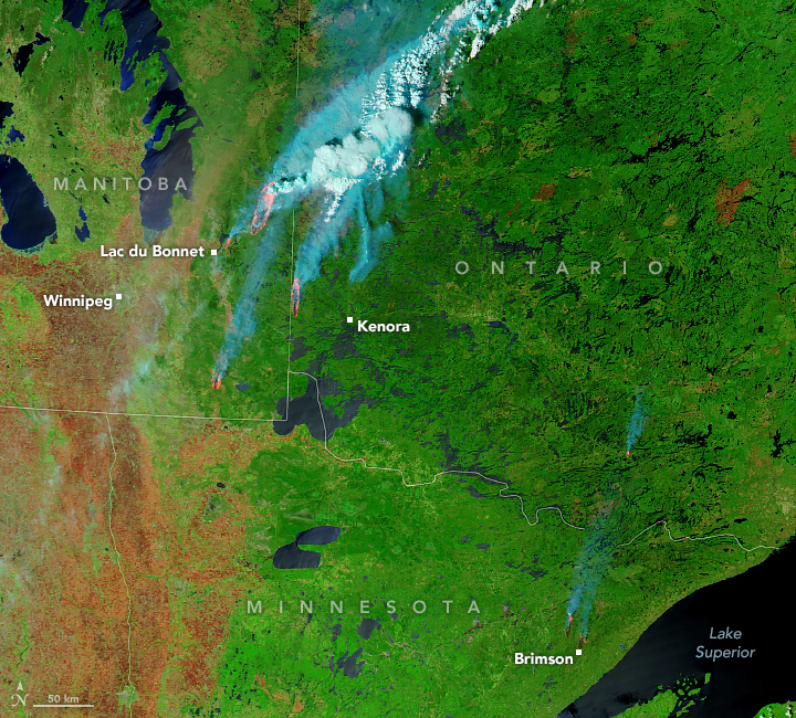 Satellite view with green and brown earth and red for fires and whitish blue for long streams of smoke.