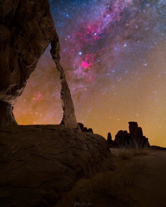Large, mostly vertical formations including a skinny rock arch in silhouette with the Milky Way behind.