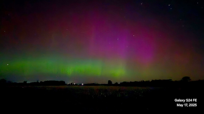 Pink and green light in vertical curtains above a dark horizon.