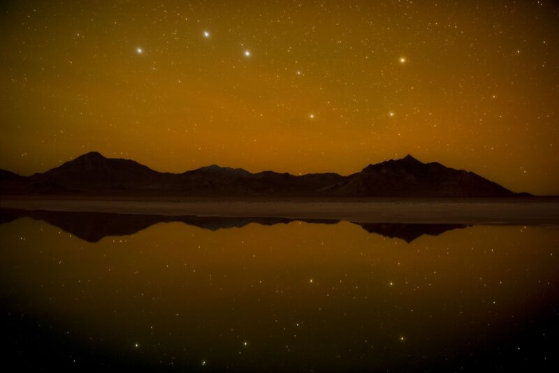 Dark, bronze colored sky with stars of the Big Dipper reflected in water below.