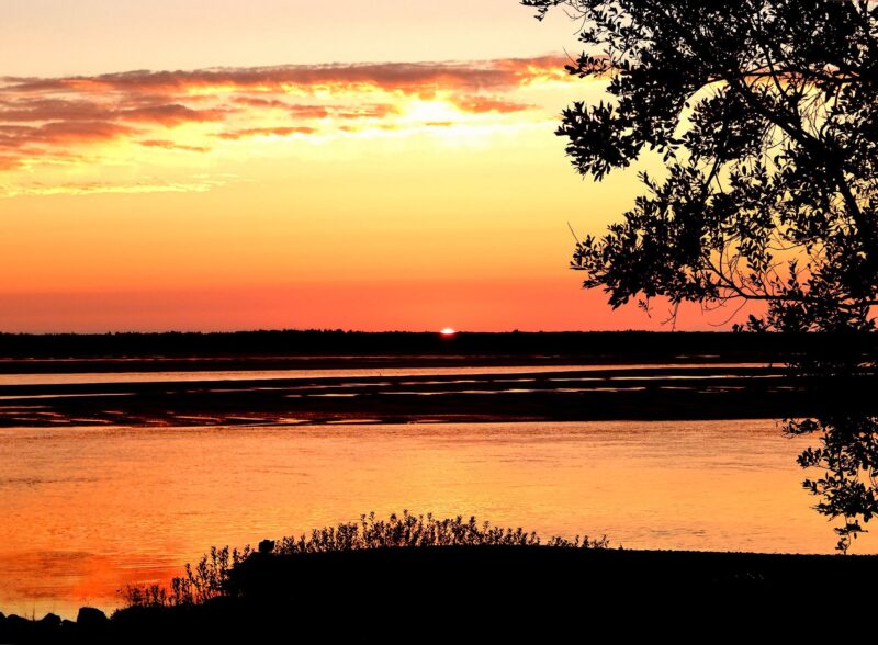 An orange sunset right over an inlet in the ocean.