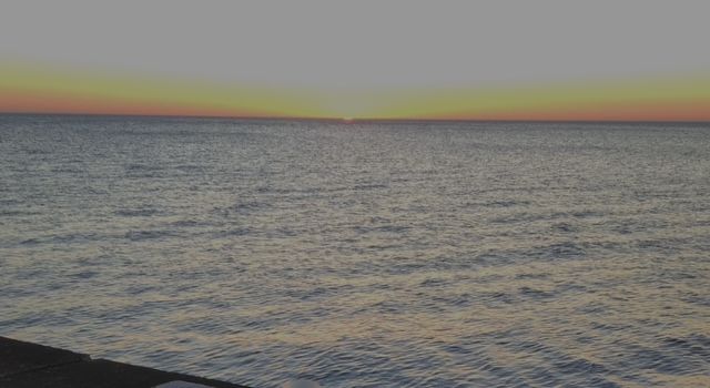 The sea with the sun rising in the distance. The horizon looks orange and yellow.