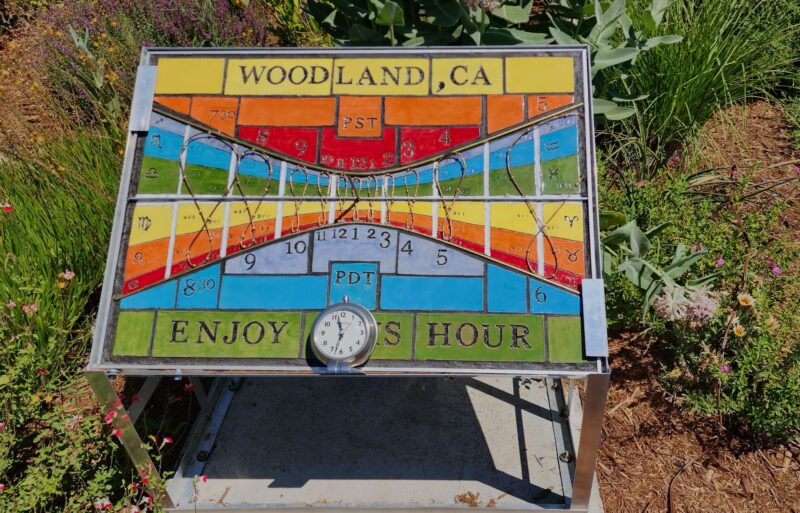 A large, rectangular, colorful ceramic sundial placed on the ground over short vegetation.
