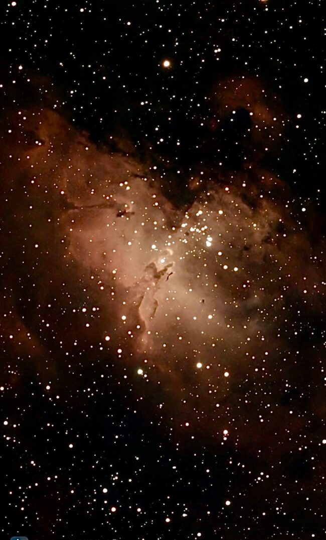 A bright orange, nebulous region with dark lanes, over a rich background of stars.