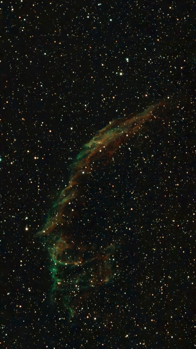 A large filament of green and orange nebulosity with a hundreds of foreground stars.