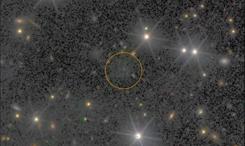 Dark galaxy: Black background with scattered foreground stars and a gray area at middle circled in yellow.