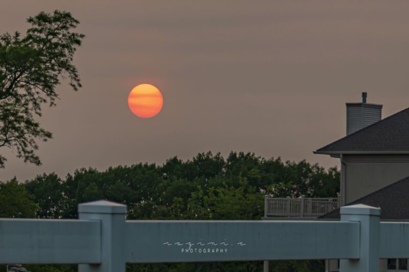 Orange sun with red bands crossing it horizontally and gray sky.