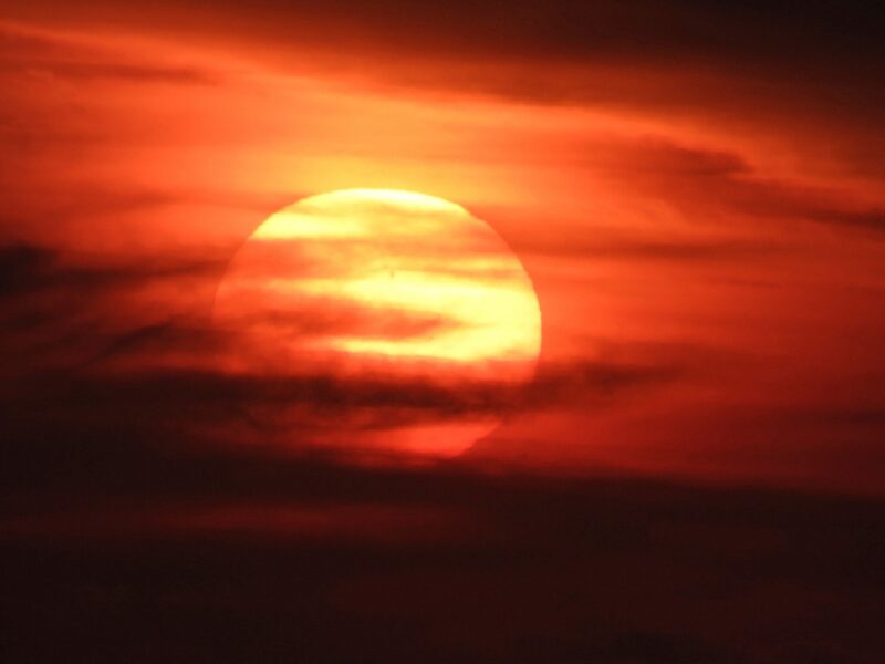 An orange sun covered in clouds. The sky looks reddish.
