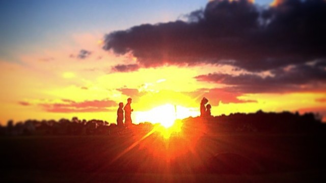 An orange glow from the sun near the horizon. There are 2 people on each side of the glow.