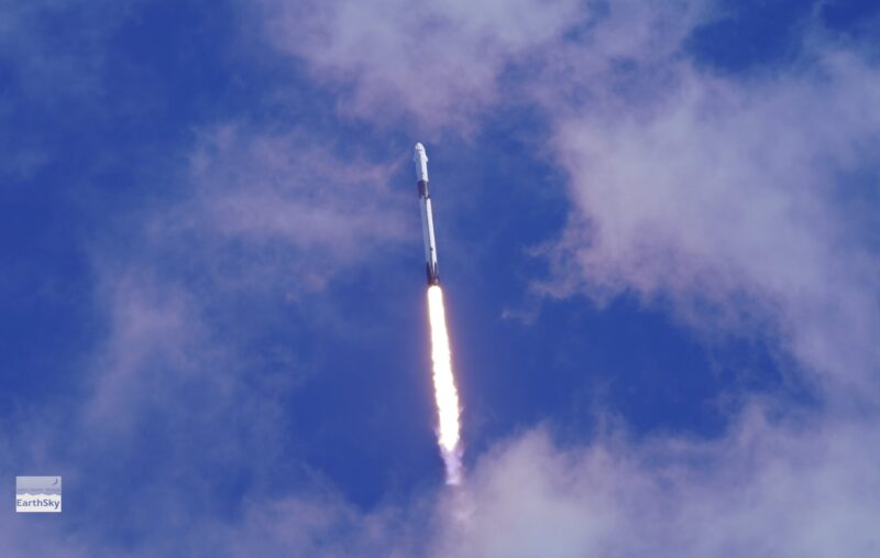 A rocket soaring into a partly cloudy sky with flame at the bottom.