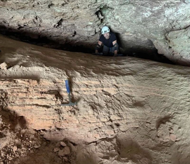 A man on a rock ledge, with an area of sedimentary rock below.