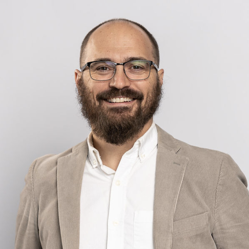 Smiling man with eyeglasses, beard and white shirt with tan corduroy jacket.