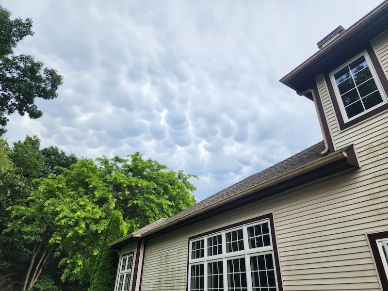 A house and trees in the foreground with with a sky full of mammatus clouds above.