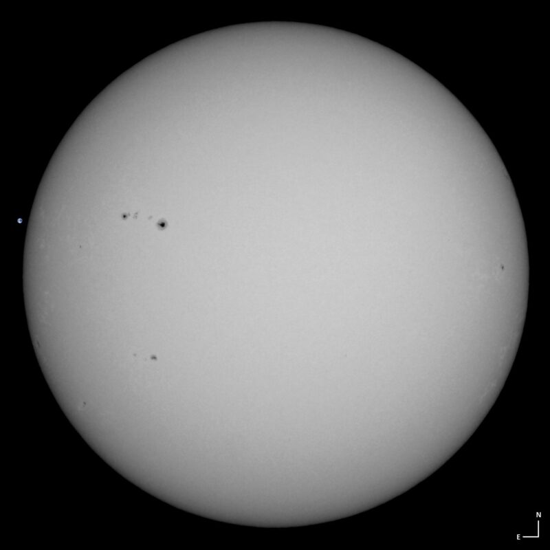 The sun, seen as a large white sphere with small dark spots.