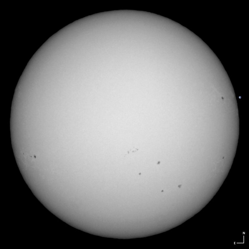 The sun, seen as a large white sphere with small dark spots.