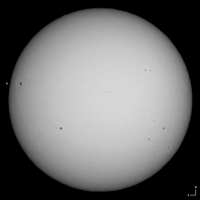 The sun, seen as a large white sphere with small dark spots.