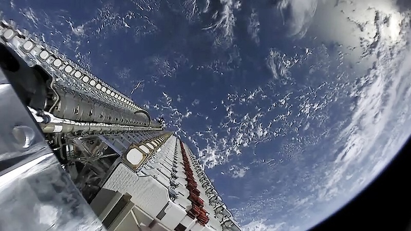 A long array of satellites in a rocket cargo bay with the Earth in the background.