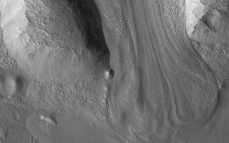 Glaciers on Mars: Black and white orbital view of a rounded flow of material on between 2 ridges on gray landscape.