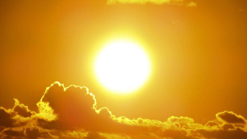 Extreme heat: The blazing sun in a yellow sky over a line of silhouetted clouds rimmed in glowing gold.
