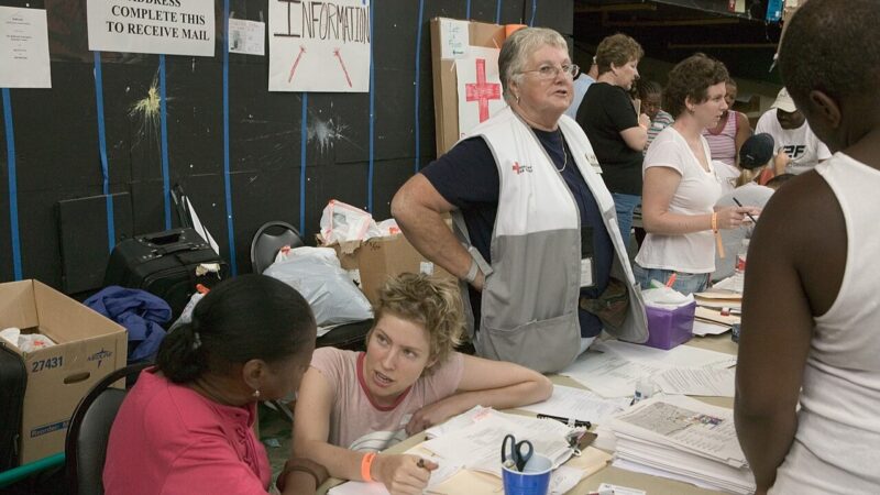 Red Cross people behind a table covered with stacks of papers, with more people on the other side.