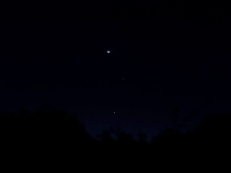 Dark sky with a thin moon at top, with 2 bright dots below, forming a line.