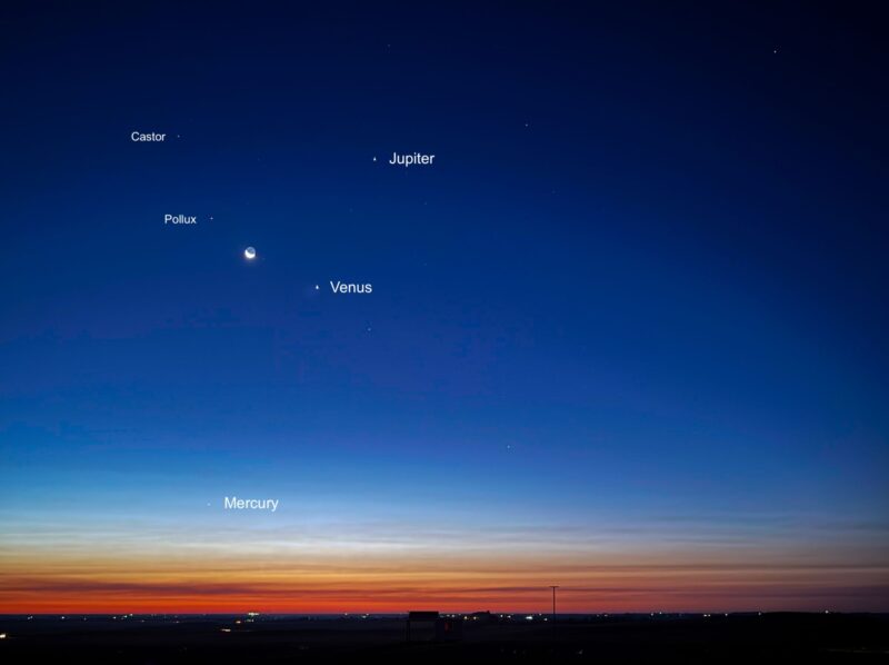 Morning planets parade: Blue sky and orange horizon. Planets, moon, and stars are high in the sky, except for Mercury, low on the horizon.
