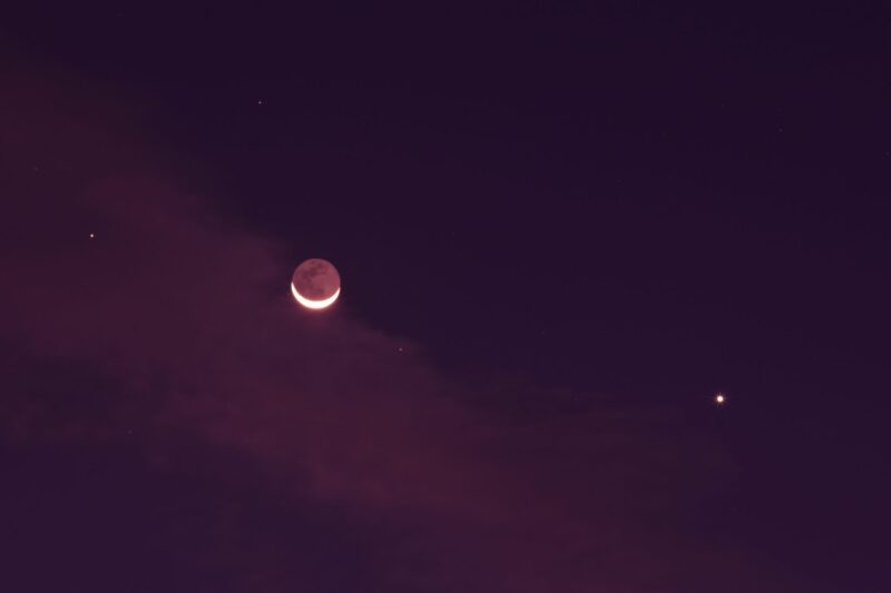 Deep pink sky with a thin crescent moon, very bright Venus and other white dots.