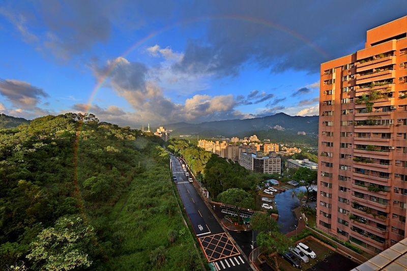 View of a big city and green hillside with an almost full rainbow showing.