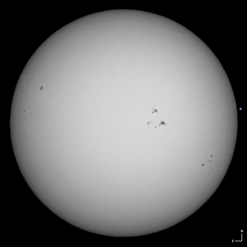 The sun, seen as a large white sphere with small dark spots.