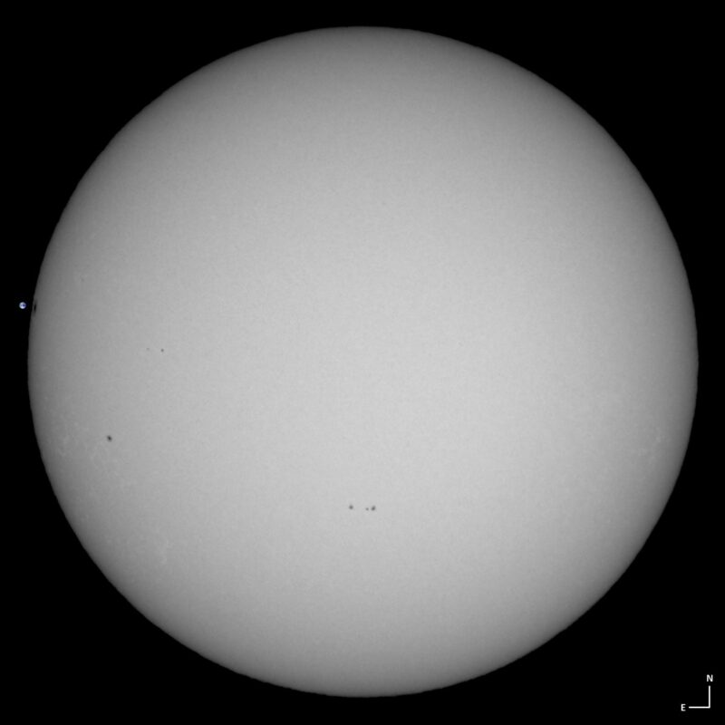 The sun, seen as a large white sphere with small dark spots.