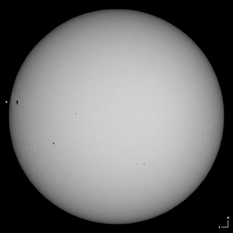 The sun, seen as a large white sphere with small dark spots.