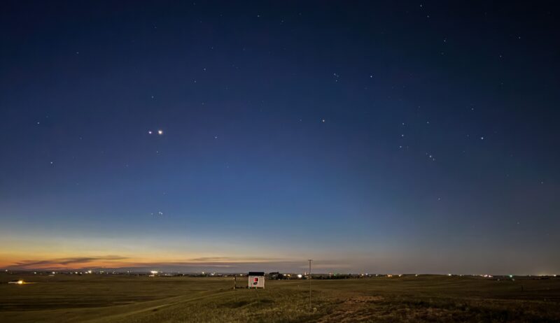 Dark blue sky with many stars. There are 2 bright dots for Jupiter and Venus on the left side. The horizon looks orangish.