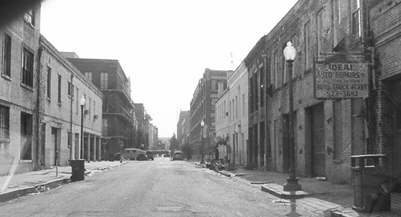 Black and white photo of an empty street stretching into the distance and military vehicles at a distant cross-street.