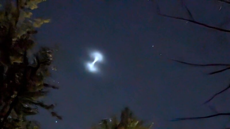 A dumbbell shaped light in the night sky.
