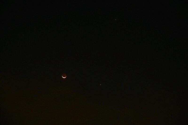 Dark sky with extremely thin moon and 2 bright dots, on to the top right, and another on the right side.