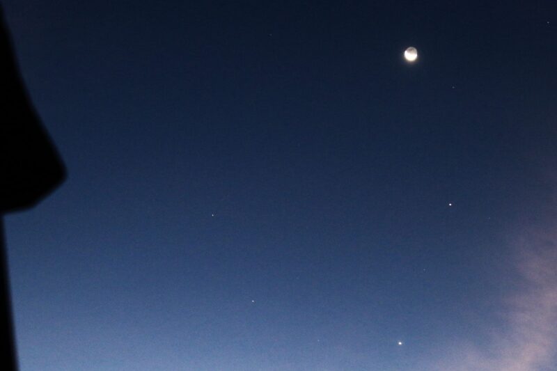 Dark blue sky with the moon at top and 2 bright dots below, forming a curved line.