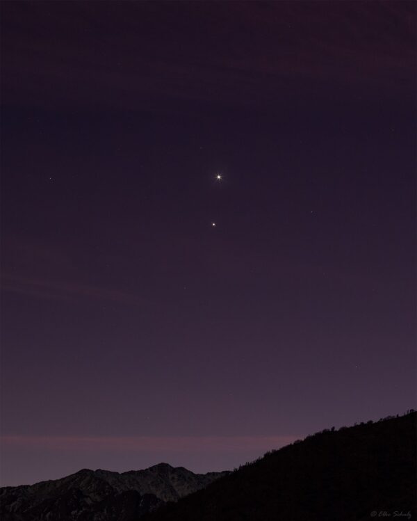 Pinkish sky with 2 dots shining bright above a mountain.