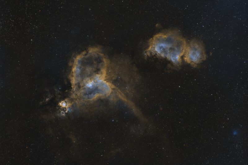 Two large, complex, yellowish swirls of gas with prominent dark lanes and numerous foreground stars.