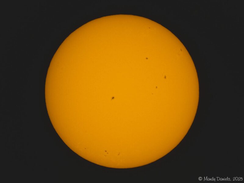 The sun, seen as a large yellow sphere with small dark spots.