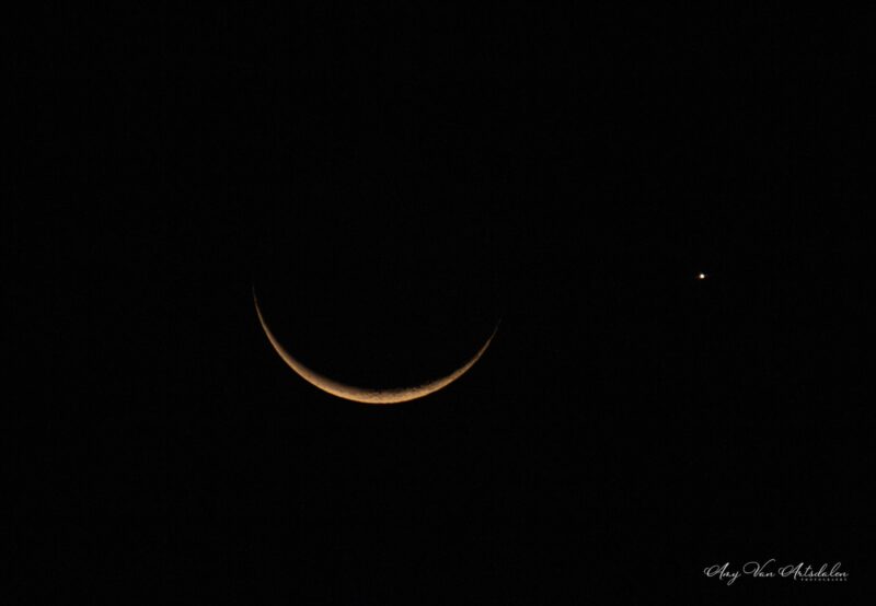 Slim, dim orange crescent moon and one bright dot to its right.