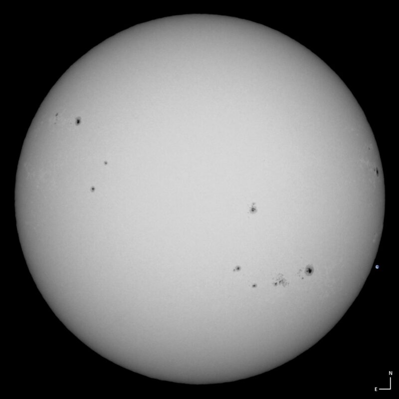 The sun, seen as a large white sphere with small dark spots.