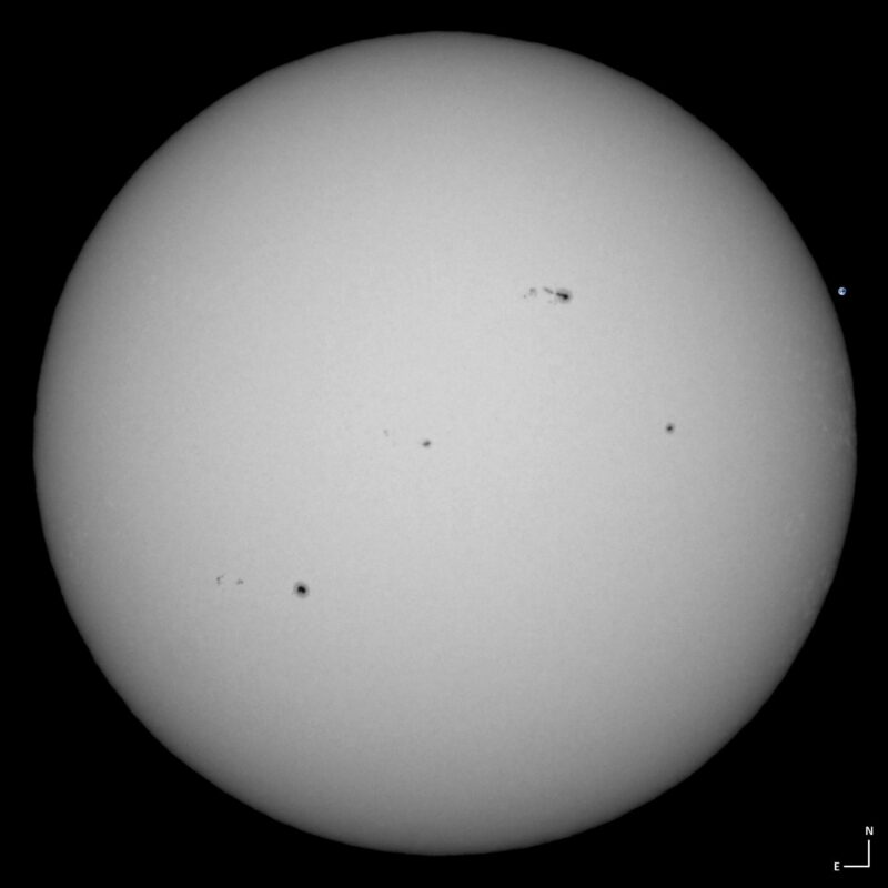 The sun, seen as a large white sphere with small dark spots.
