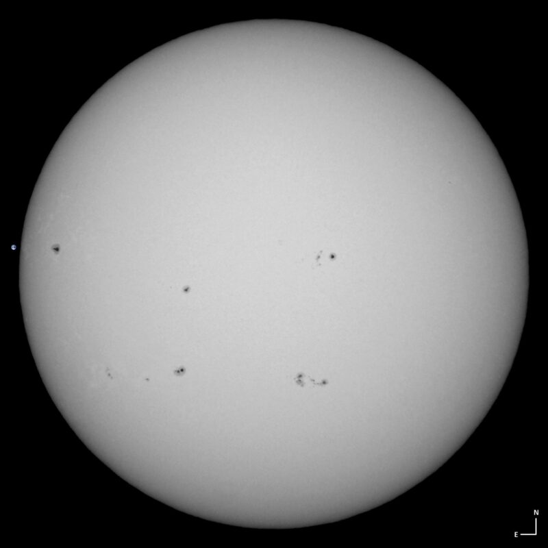 The sun, seen as a large white sphere with small dark spots.